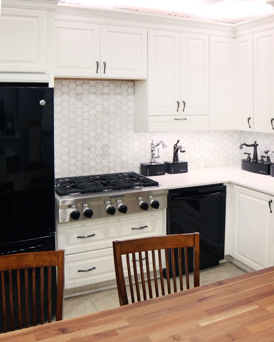 A modern kitchen with white cabinets, a black refrigerator, gas stove, black dishwasher, wooden chairs, and a hexagonal tile backsplash showcases 2020 kitchen design trends. The countertop features a coffee maker and decorative items. A modern kitchen with white cabinets, a black refrigerator, gas stove, black dishwasher, wooden chairs, and a hexagonal tile backsplash showcases 2020 kitchen design trends. The countertop features a coffee maker and decorative items.