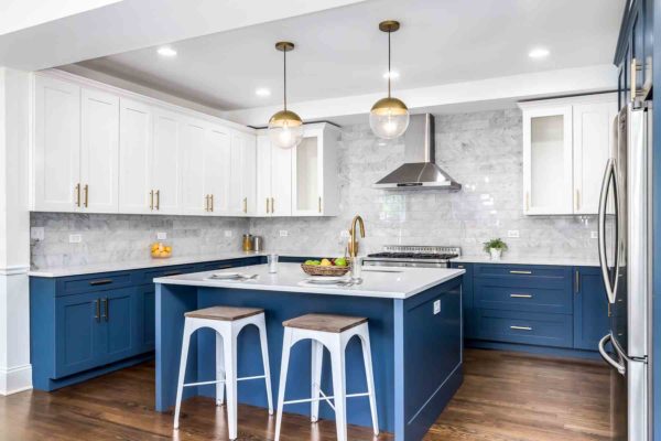 Modern kitchen design with blue lower cabinets, white uppers, marble backsplash, stainless steel appliances, and a stylish center island with stools. A reflection of 2021 kitchen design trends, with fruit bowls adorning the counters and pendant lights overhead. Modern kitchen design with blue lower cabinets, white uppers, marble backsplash, stainless steel appliances, and a stylish center island with stools. A reflection of 2021 kitchen design trends, with fruit bowls adorning the counters and pendant lights overhead.