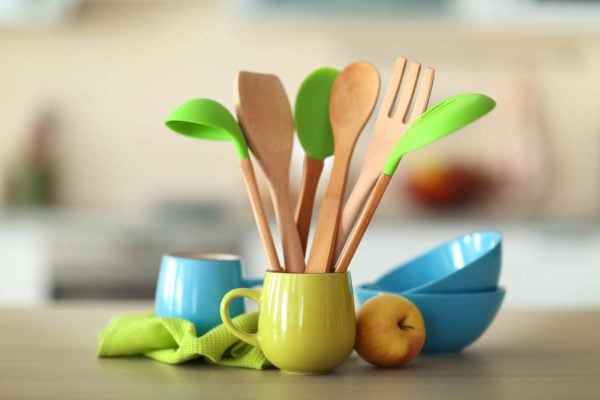 A yellow mug holds various wooden and green silicone kitchen utensils on a kitchen counter, reflecting 2021 Kitchen Design Trends, with blue bowls, a blue mug, a green cloth, and an apple nearby. A yellow mug holds various wooden and green silicone kitchen utensils on a kitchen counter, reflecting 2021 Kitchen Design Trends, with blue bowls, a blue mug, a green cloth, and an apple nearby.