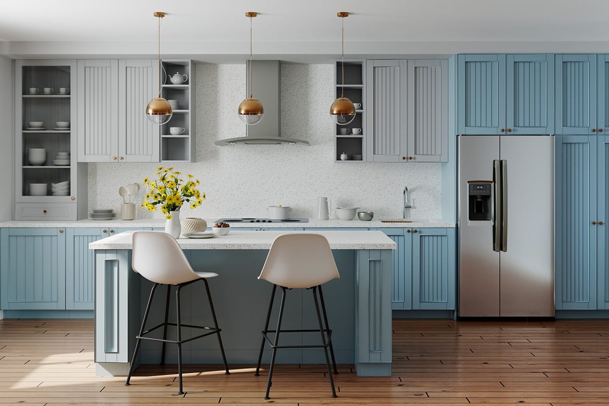 Modern kitchen makeover featuring blue and white cabinets, a large island with two white chairs, stainless steel appliances, wooden floor, and three pendant lights. A vase of yellow flowers adds a pop of color to update the kitchen.