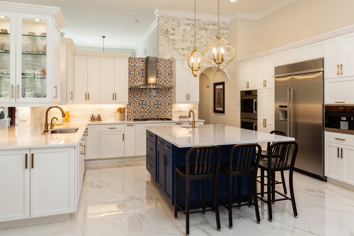 Modern kitchen design with white cabinets, stainless steel appliances, a large island with a blue base and three black chairs, marble floors, and two gold chandeliers. The decorative tile backsplash highlights popular kitchen layouts. Modern kitchen design with white cabinets, stainless steel appliances, a large island with a blue base and three black chairs, marble floors, and two gold chandeliers. The decorative tile backsplash highlights popular kitchen layouts.