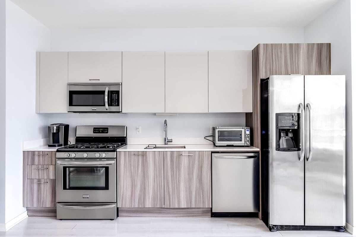 Modern kitchen with stainless steel appliances, including a refrigerator, dishwasher, oven, and microwave. Light wood and white cabinets are complemented by a white countertop—an excellent example of contemporary kitchen design layouts. Coffee maker and toaster included. Modern kitchen with stainless steel appliances, including a refrigerator, dishwasher, oven, and microwave. Light wood and white cabinets are complemented by a white countertop—an excellent example of contemporary kitchen design layouts. Coffee maker and toaster included.