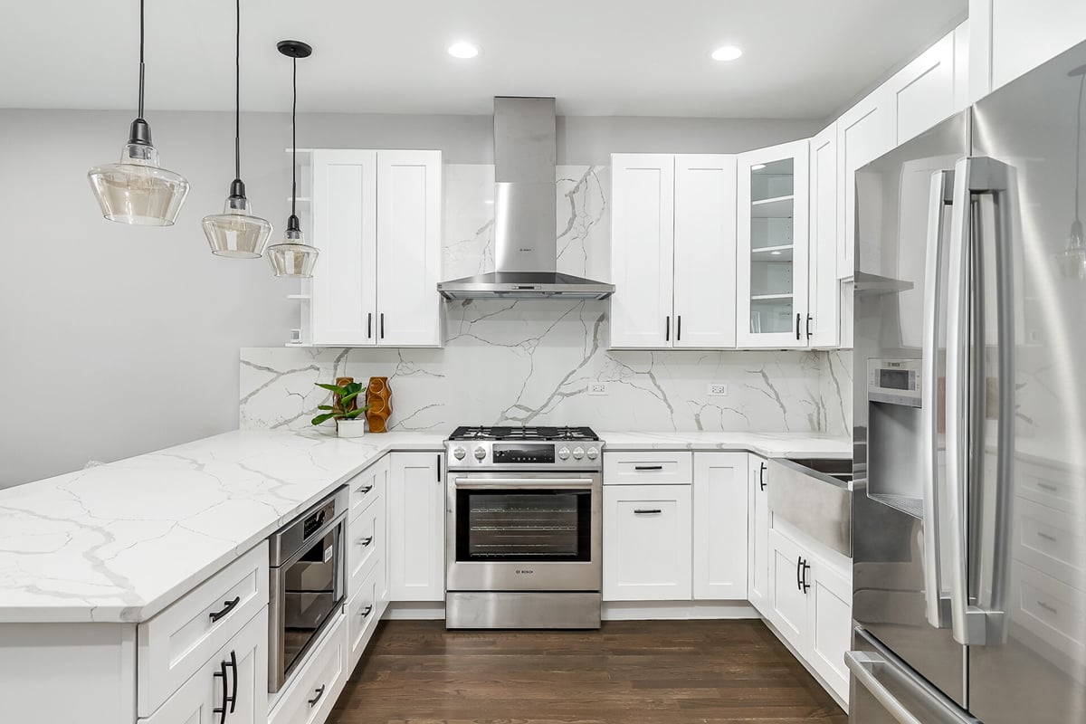 Modern kitchen design with white cabinets, stainless steel appliances, marble countertops and backsplash, pendant lights, and a farmhouse sink—all showcasing one of today’s most popular kitchen layouts on a dark wood floor. Modern kitchen design with white cabinets, stainless steel appliances, marble countertops and backsplash, pendant lights, and a farmhouse sink—all showcasing one of today’s most popular kitchen layouts on a dark wood floor.