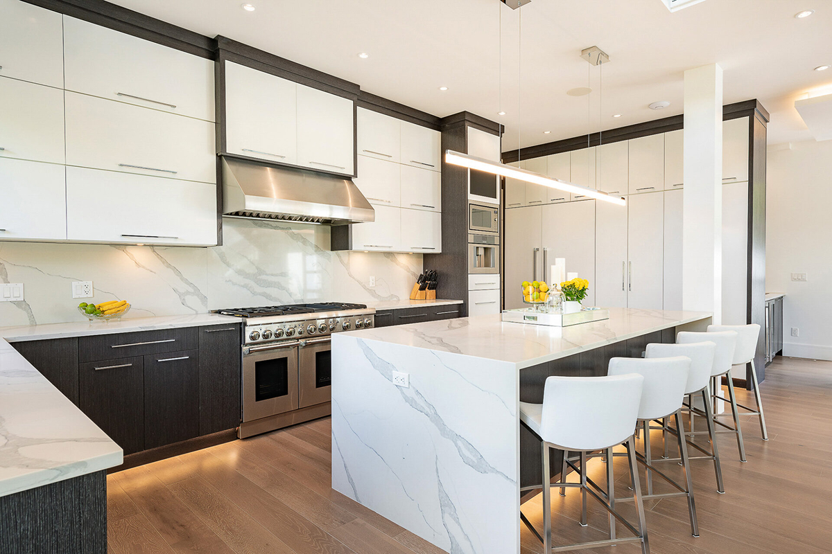 Modern kitchen with white and dark cabinets, marble countertops, a stylish stone kitchen backsplash, stainless steel appliances, a large island with four white barstools, and decorative yellow accents. Modern kitchen with white and dark cabinets, marble countertops, a stylish stone kitchen backsplash, stainless steel appliances, a large island with four white barstools, and decorative yellow accents.