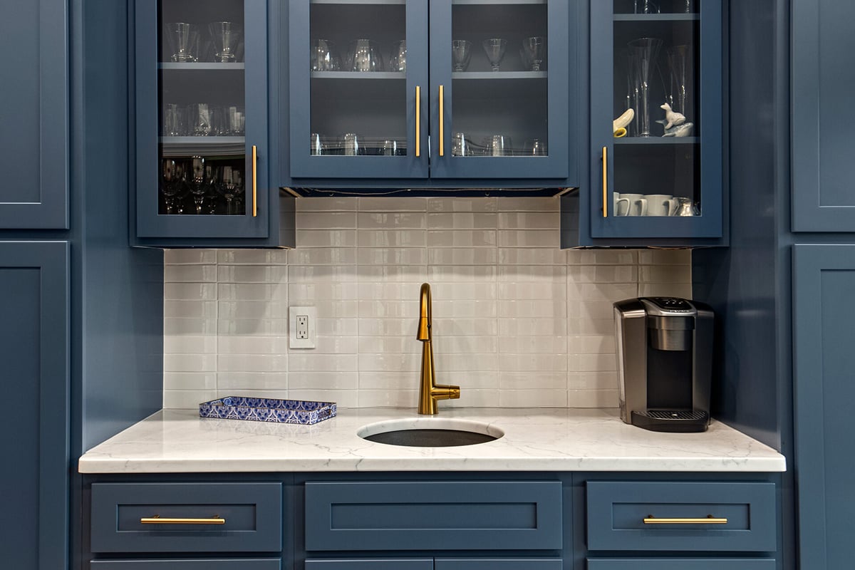 A modern kitchen area with blue cabinets, gold handles, a gold faucet over a small round sink—perfect as a wet bar. Features include a white tile backsplash, marble countertop, coffee maker, and patterned tissue box. A modern kitchen area with blue cabinets, gold handles, a gold faucet over a small round sink—perfect as a wet bar. Features include a white tile backsplash, marble countertop, coffee maker, and patterned tissue box.