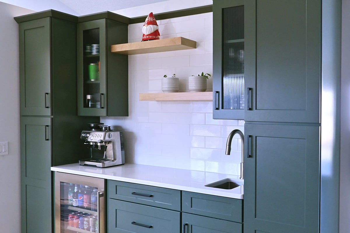 A modern kitchen nook with dark green cabinets, white countertop, built-in mini fridge, espresso machine, and open wooden shelves holding dishes, potted plants, and a decorative Santa—perfect for stress-free entertaining or holiday party prep. White tile backsplash. A modern kitchen nook with dark green cabinets, white countertop, built-in mini fridge, espresso machine, and open wooden shelves holding dishes, potted plants, and a decorative Santa—perfect for stress-free entertaining or holiday party prep. White tile backsplash.