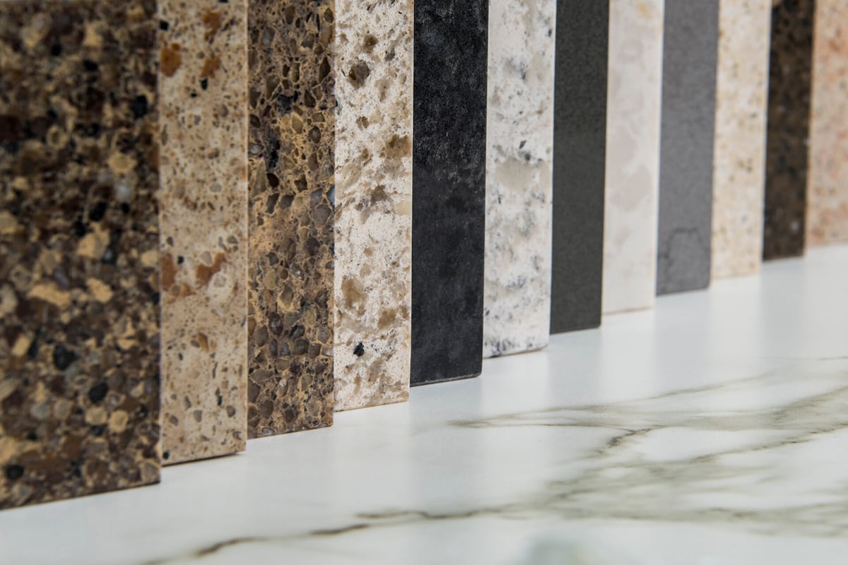 A row of upright countertop samples in various colors and textures, mostly shades of brown, beige, black, and gray, displayed on a white surface with gray veining—ideal for pairing with waterproof flooring options. A row of upright countertop samples in various colors and textures, mostly shades of brown, beige, black, and gray, displayed on a white surface with gray veining—ideal for pairing with waterproof flooring options.