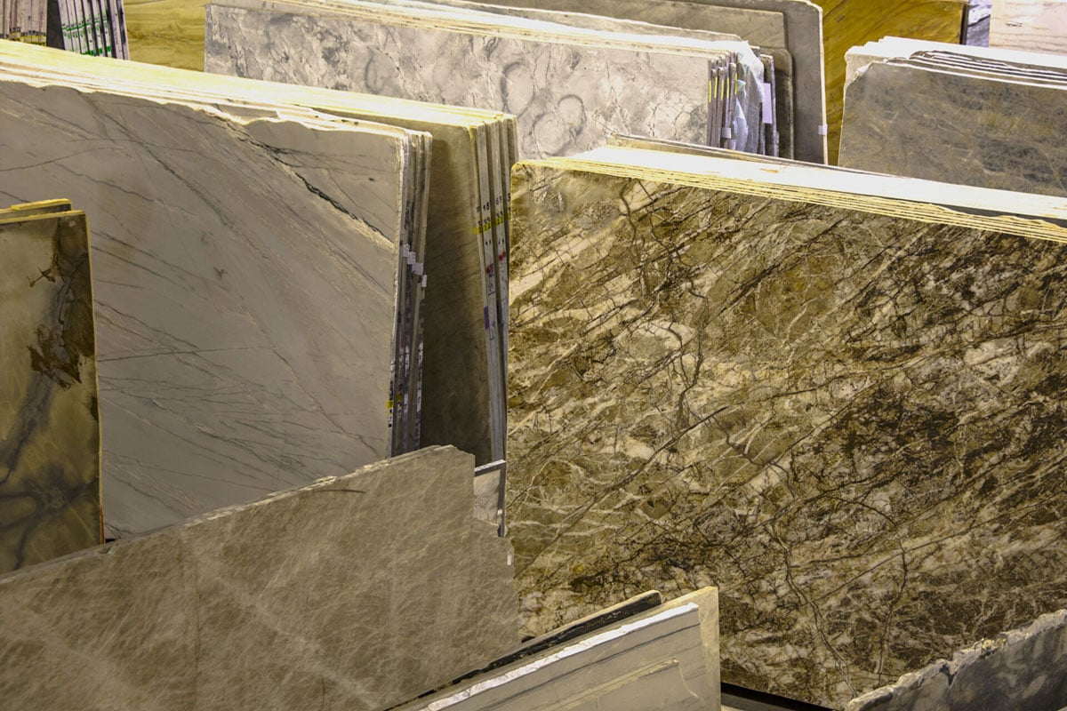 Several large slabs of natural stone, including marble and granite, are vertically displayed side by side in a showroom, highlighting various colors and veined patterns perfect for elegant flooring or water resistant flooring solutions. Several large slabs of natural stone, including marble and granite, are vertically displayed side by side in a showroom, highlighting various colors and veined patterns perfect for elegant flooring or water resistant flooring solutions.