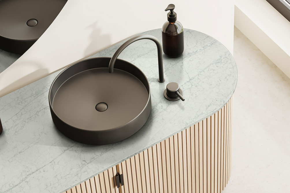 A modern bathroom sink with a round black basin, matching faucet, soap dispenser, and lever sits on a light marble countertop above a wood slat cabinet—perfect inspiration for your next kitchen remodel. A modern bathroom sink with a round black basin, matching faucet, soap dispenser, and lever sits on a light marble countertop above a wood slat cabinet—perfect inspiration for your next kitchen remodel.