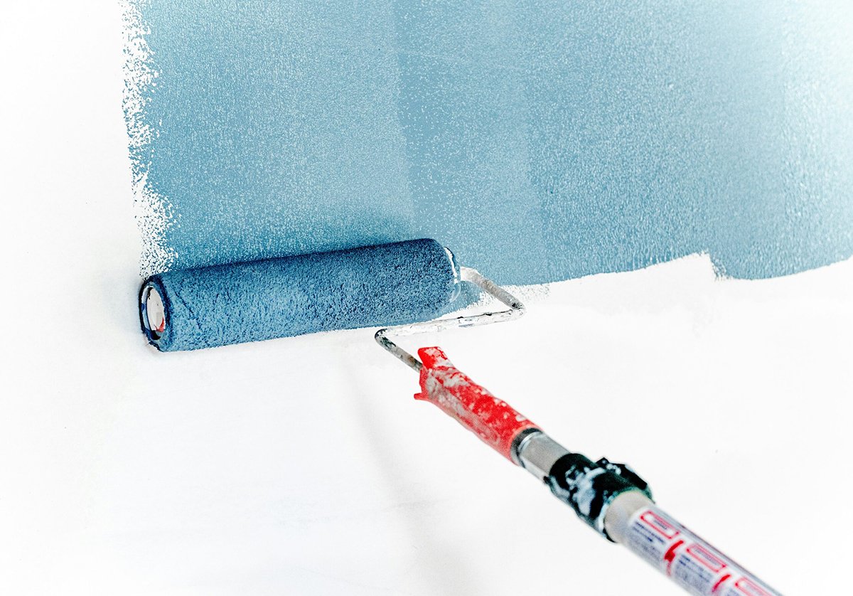 A paint roller with a red handle is applying light blue paint to a white wall, creating a smooth, even layer—perfect for a fresh kitchen remodel.