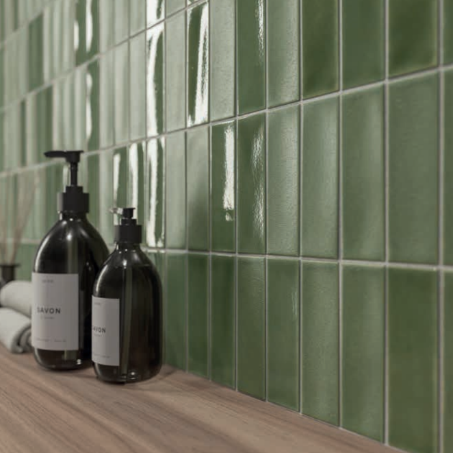Two dark pump soap bottles sit on a wooden surface in front of a wall of glossy green square tiles—an elegant detail to inspire your next kitchen remodel. A rolled towel and small container are partially visible in the background. Two dark pump soap bottles sit on a wooden surface in front of a wall of glossy green square tiles—an elegant detail to inspire your next kitchen remodel. A rolled towel and small container are partially visible in the background.