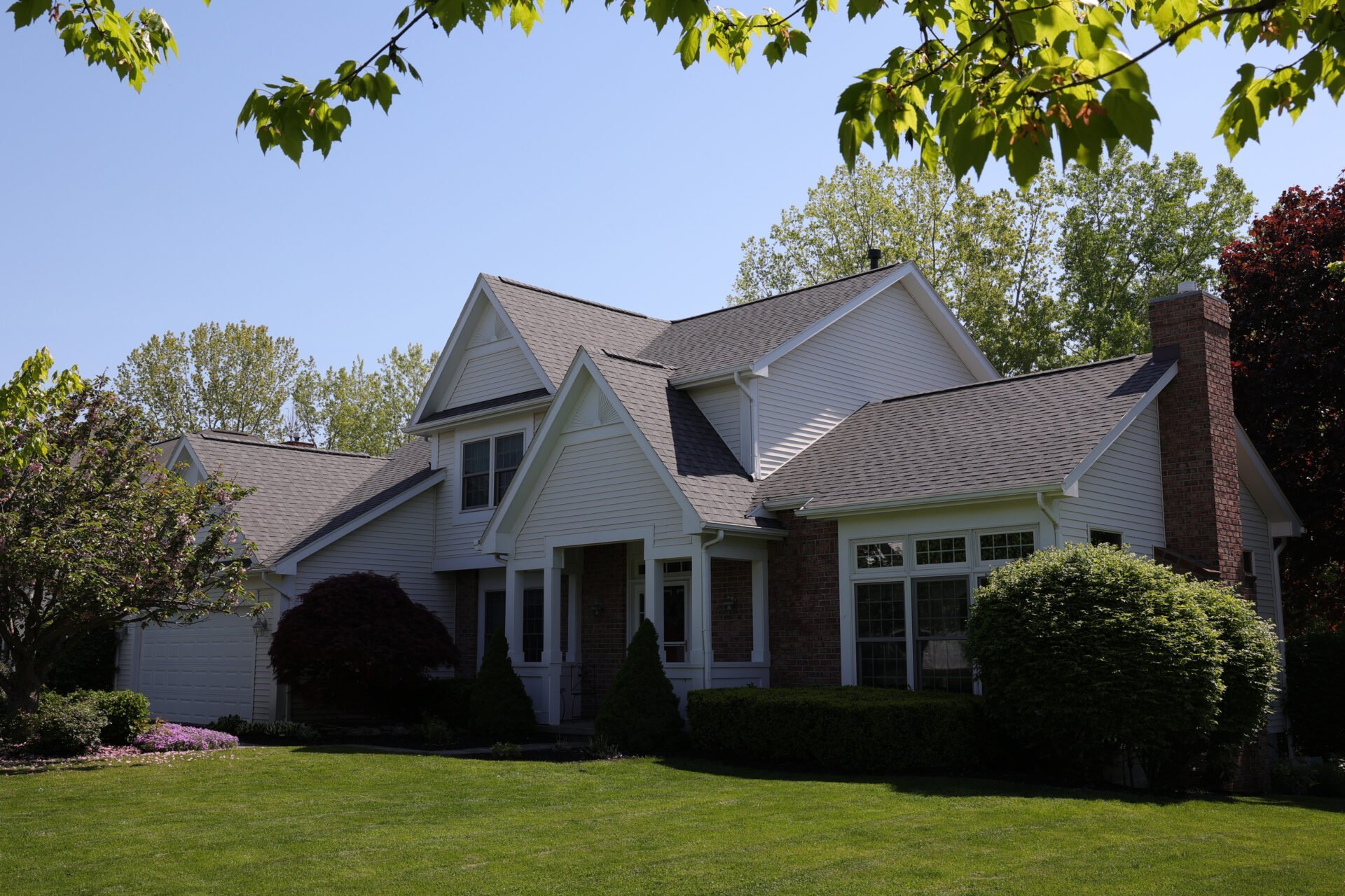 A white suburban house with multiple gables, brick accents, and a chimney, featuring a stunning kitchen remodel, is surrounded by green trees, bushes, and a neatly trimmed lawn under a clear blue sky. A white suburban house with multiple gables, brick accents, and a chimney, featuring a stunning kitchen remodel, is surrounded by green trees, bushes, and a neatly trimmed lawn under a clear blue sky.