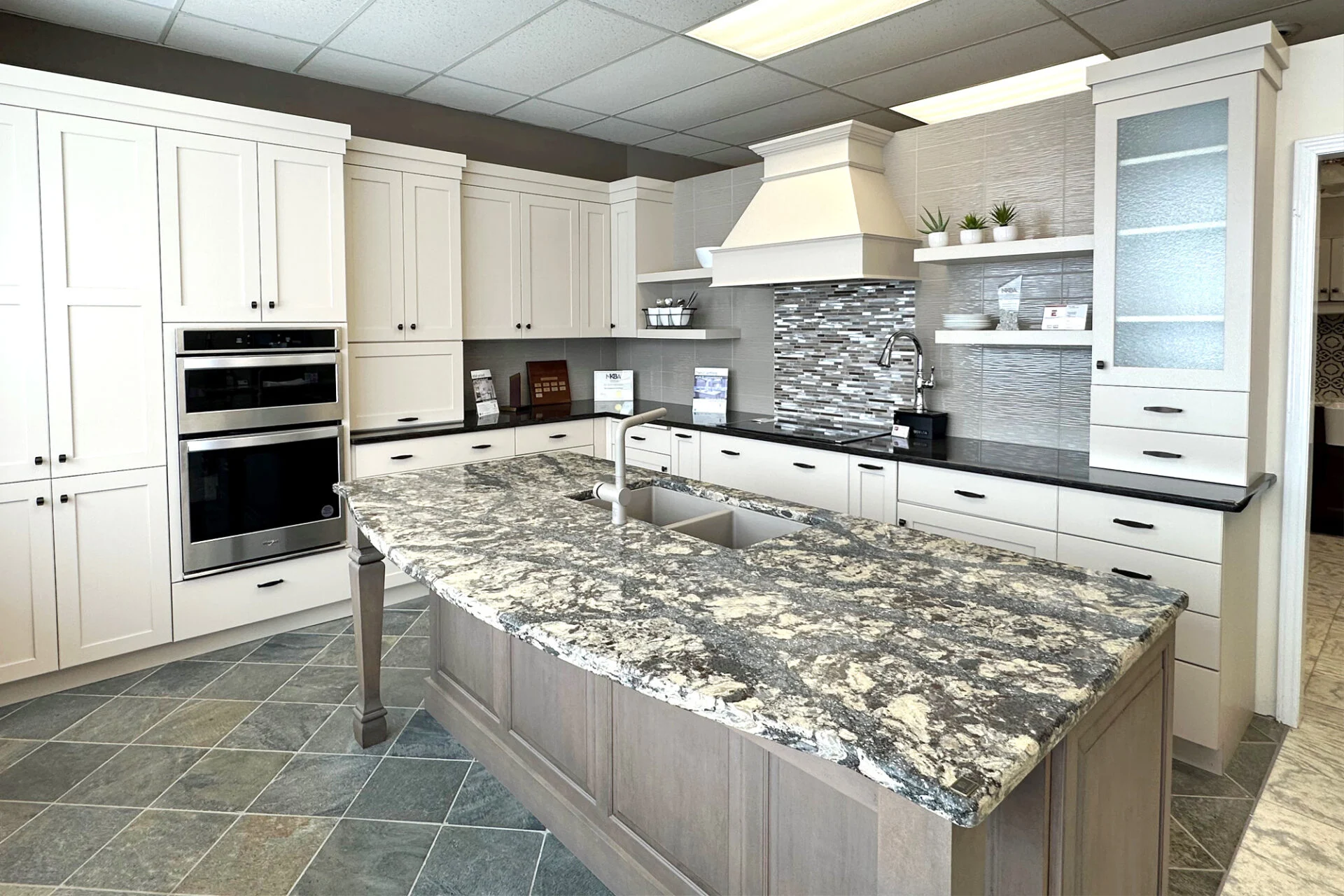 Modern kitchen remodel with white cabinets, gray and white granite island, stainless steel appliances, mosaic tile backsplash, and open shelves featuring small plants and decor. Tile flooring and under-cabinet lighting complete the look. Modern kitchen remodel with white cabinets, gray and white granite island, stainless steel appliances, mosaic tile backsplash, and open shelves featuring small plants and decor. Tile flooring and under-cabinet lighting complete the look.