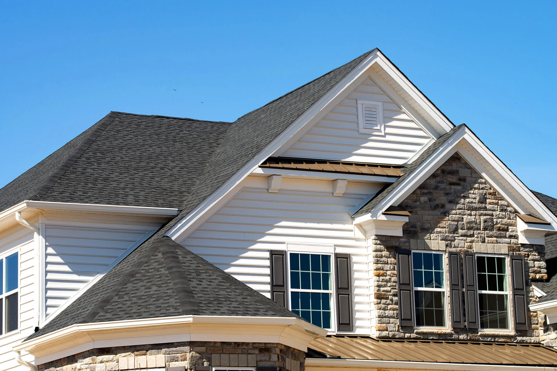 A close-up view of a house exterior featuring gray asphalt shingle roofing, white siding, and stone accents—perfect inspiration for your next kitchen remodel—plus double-hung windows with dark shutters set against a clear blue sky. A close-up view of a house exterior featuring gray asphalt shingle roofing, white siding, and stone accents—perfect inspiration for your next kitchen remodel—plus double-hung windows with dark shutters set against a clear blue sky.