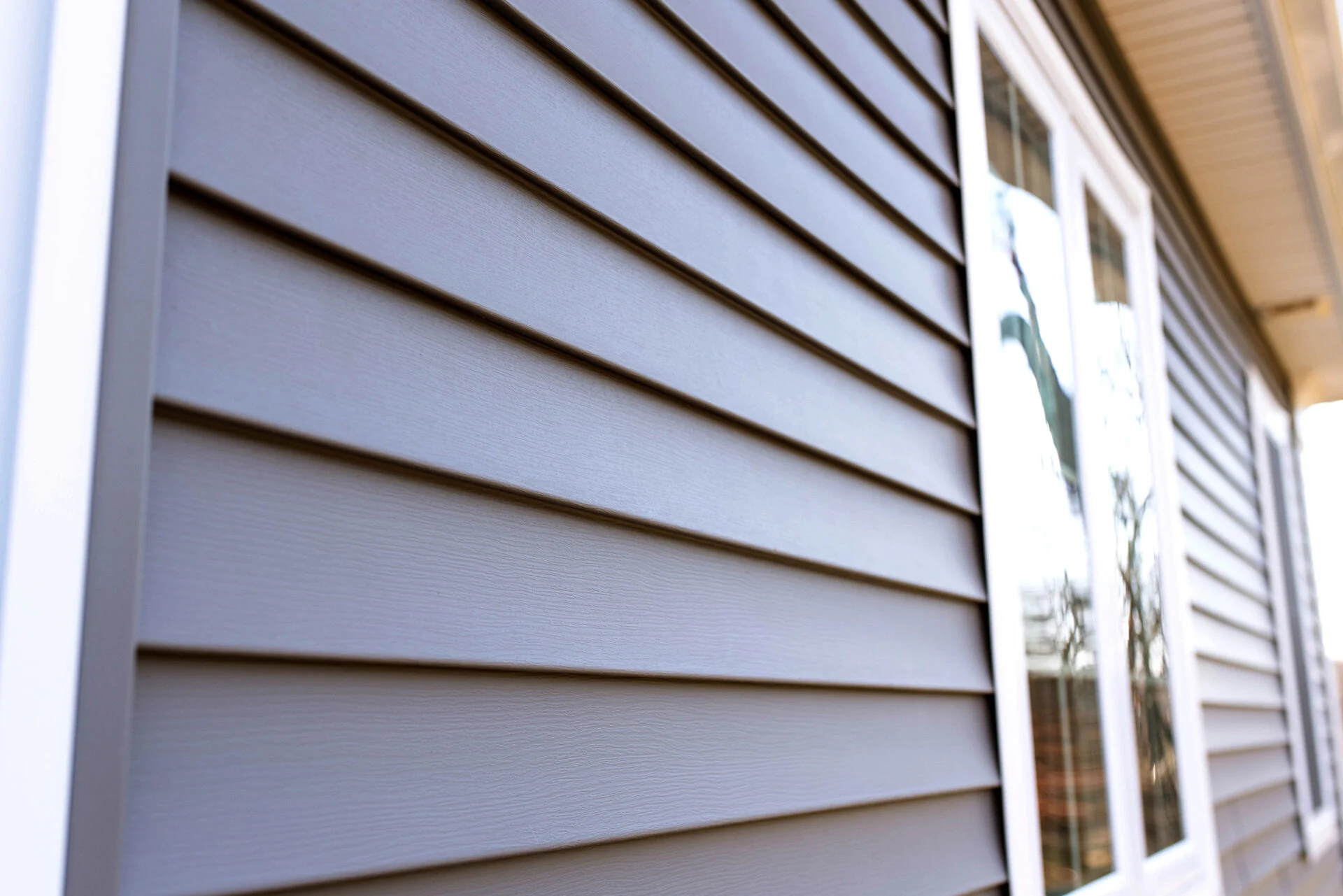 Close-up view of gray horizontal vinyl siding on a house exterior, with part of a white-trimmed window reflecting trees and sky—an inviting look perfect for showcasing your kitchen remodel inside. Close-up view of gray horizontal vinyl siding on a house exterior, with part of a white-trimmed window reflecting trees and sky—an inviting look perfect for showcasing your kitchen remodel inside.