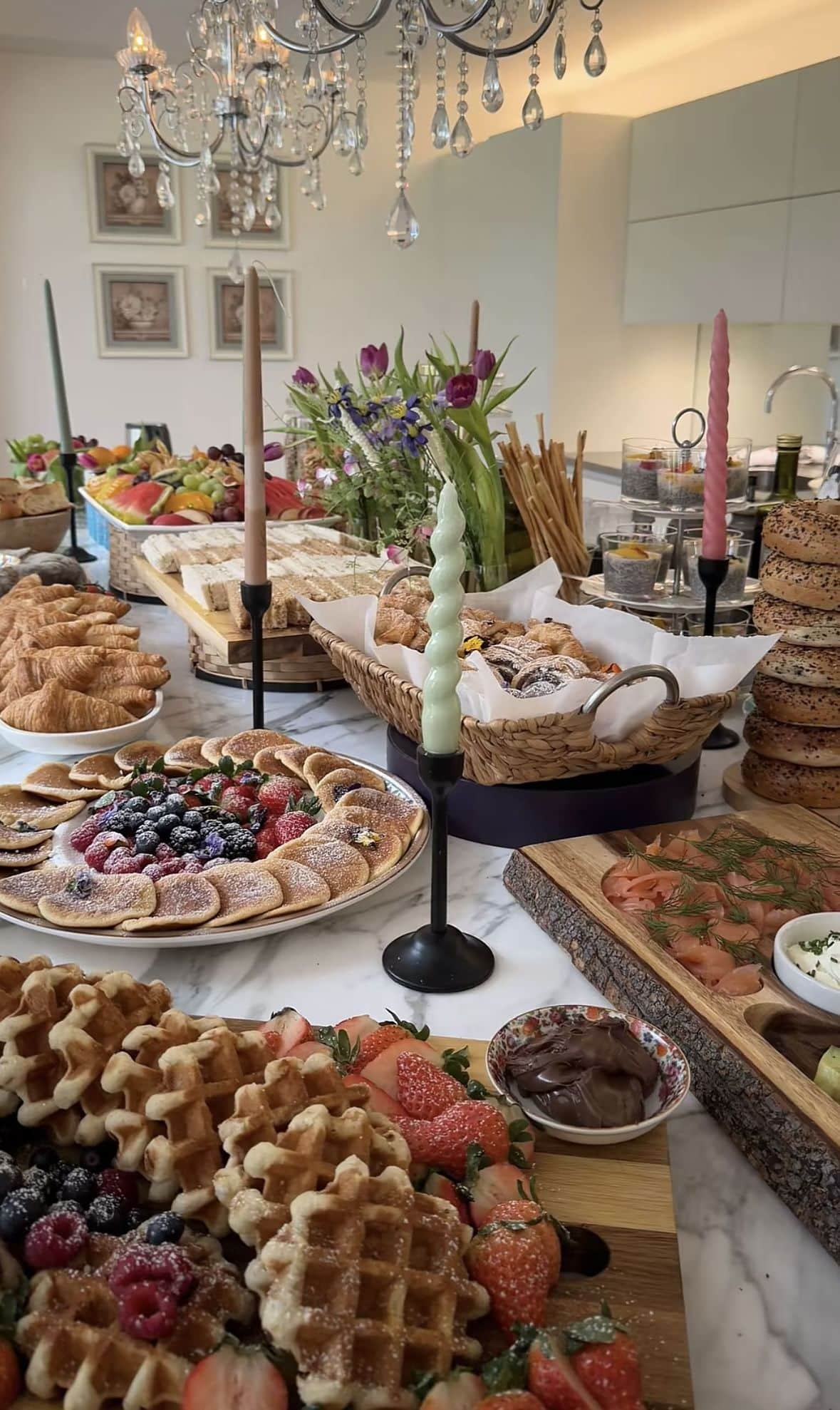 A spread of breakfast foods including waffles, pastries and fruit. The table is set with various dishes and decorations.