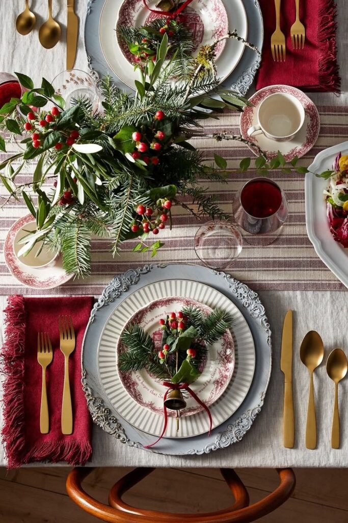 A beautifully set table with plates, gold cutlery, and a festive Christmas arrangement.
