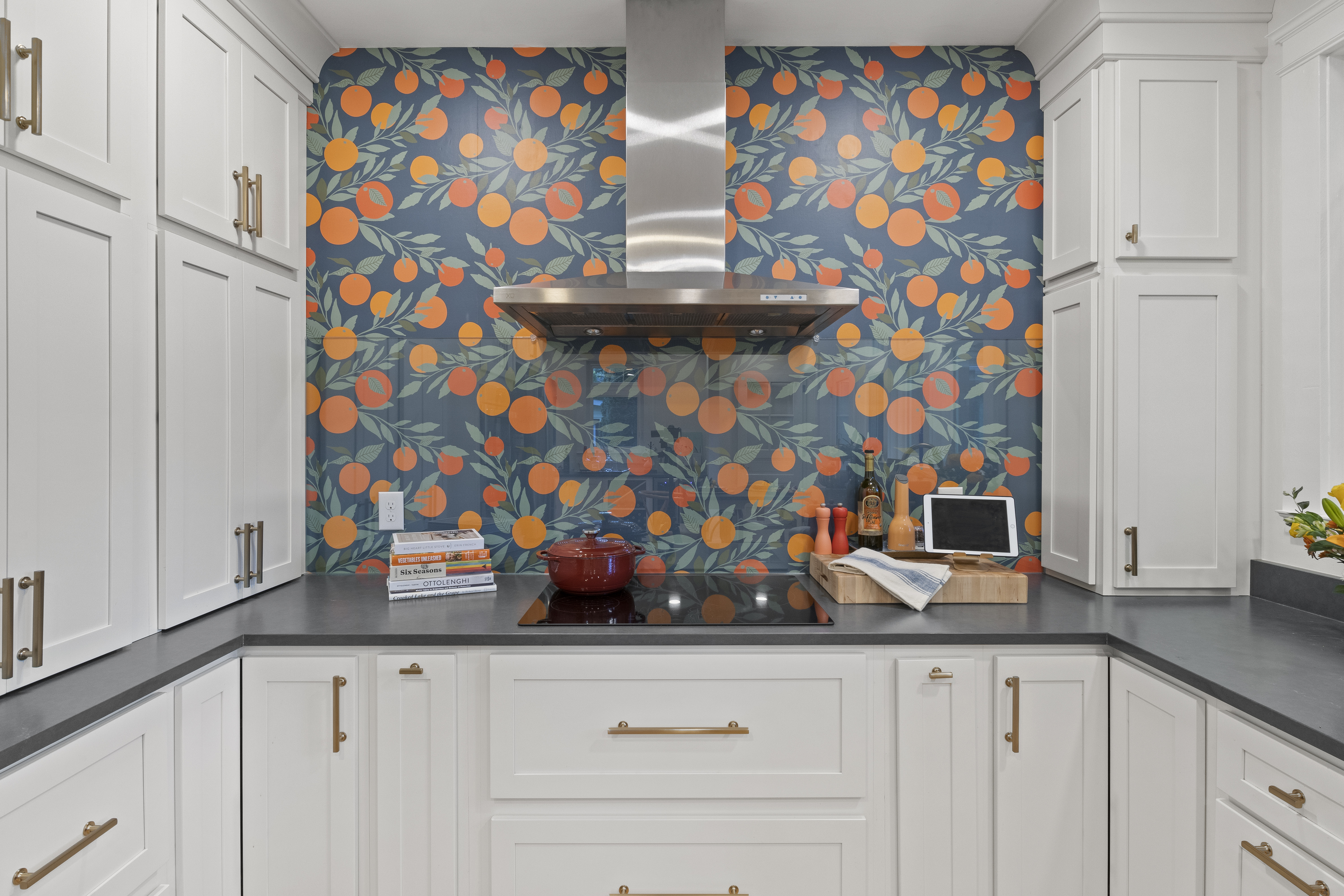 A modern kitchen with white cabinets and a blue backsplash with orange flowers. The kitchen has a stainless steel range hood and black countertops.