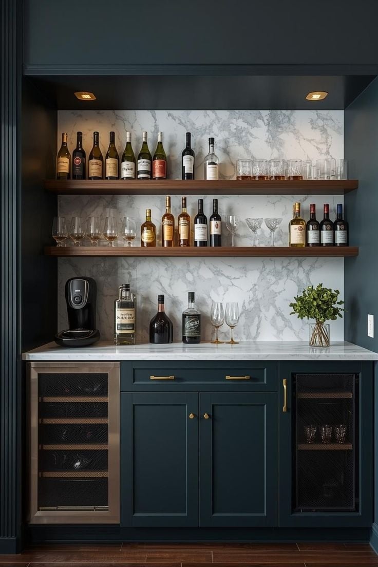 A stylish home bar with wine bottles, glasses, and a coffee maker on a marble backsplash.