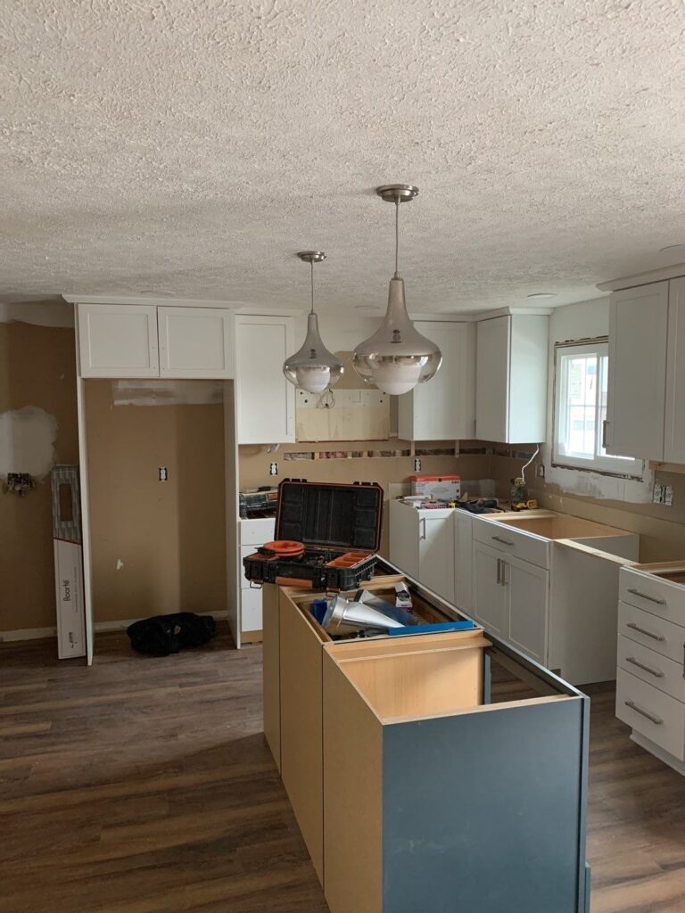 Kitchen renovation with tools on the counter. The room has white cabinets and brown countertops.