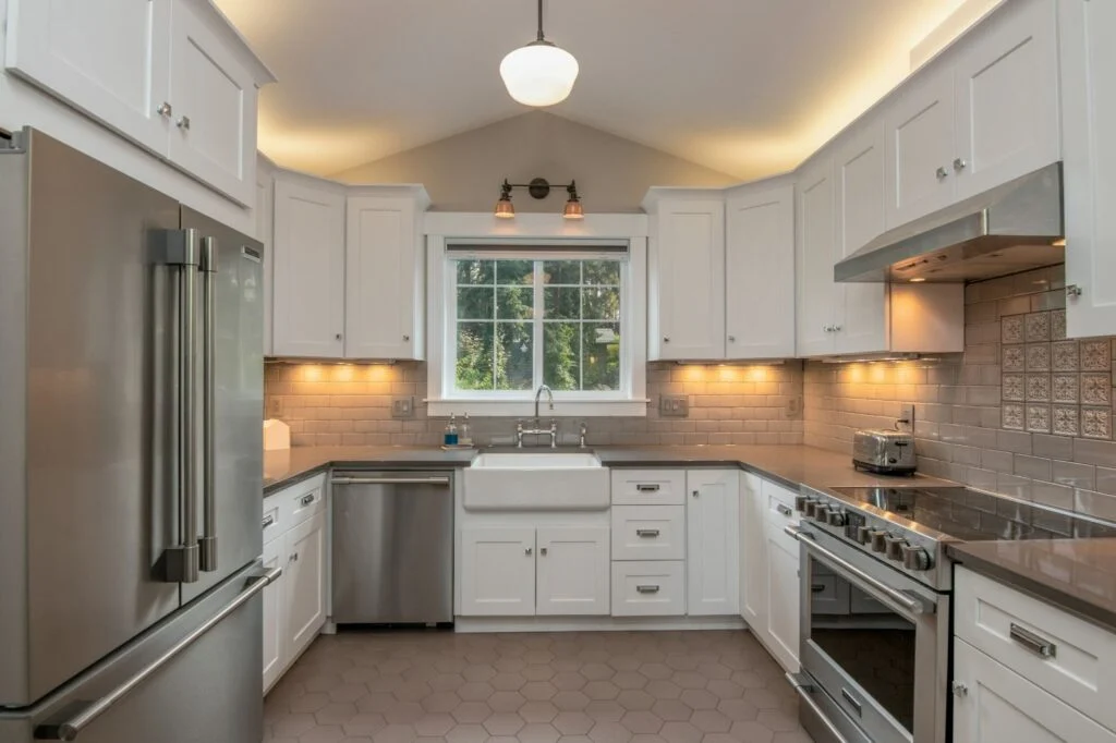 A kitchen with white cabinets, stainless steel appliances, and a window above the sink