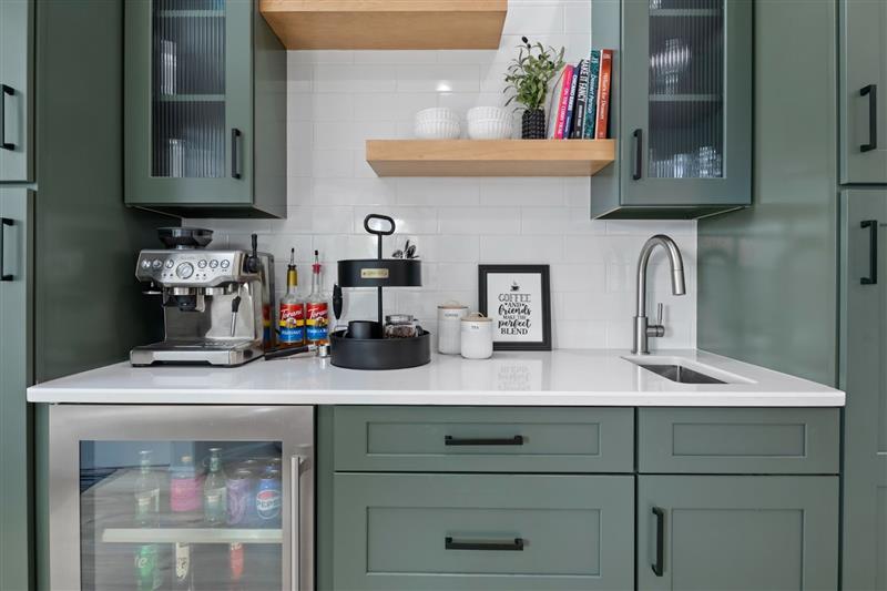 A kitchen counter with coffee maker and sink. The kitchen has green cabinets and a white countertop.