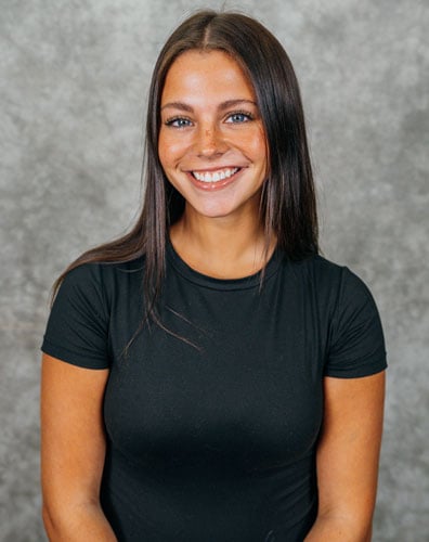 A young woman with long brown hair wearing a black t-shirt. She is smiling and looking at the camera.