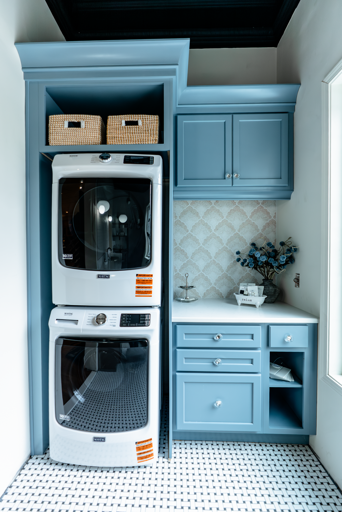 A laundry room with blue cabinets and a stacked washer and dryer. The room has a white and black checkered floor.