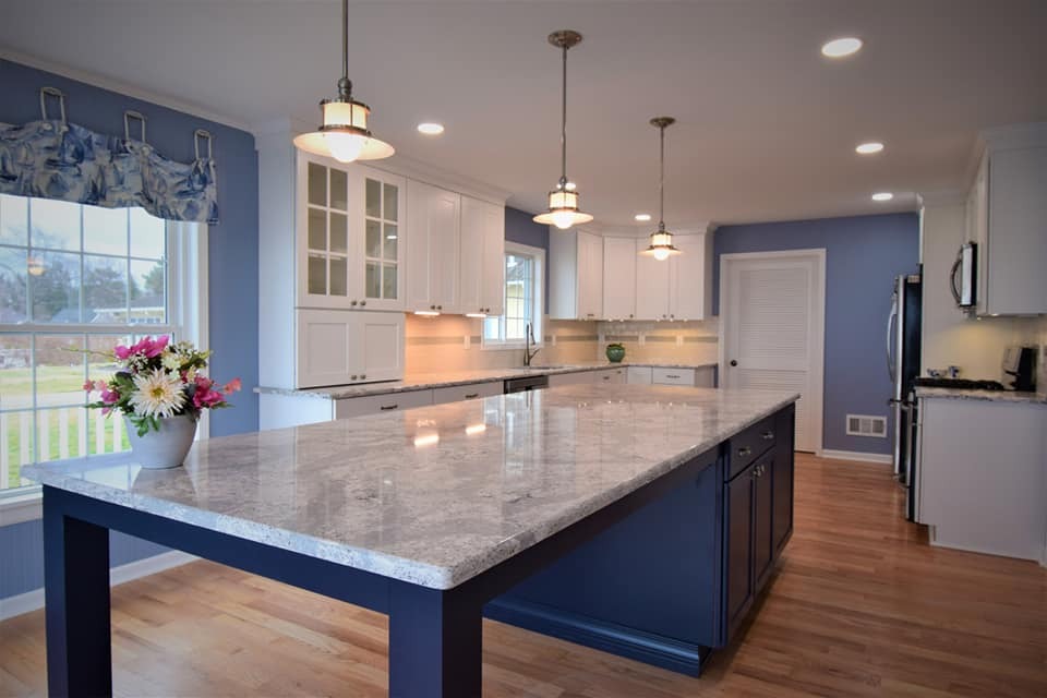 A kitchen with a large island, white cabinets, and blue walls. A vase with flowers on the island.