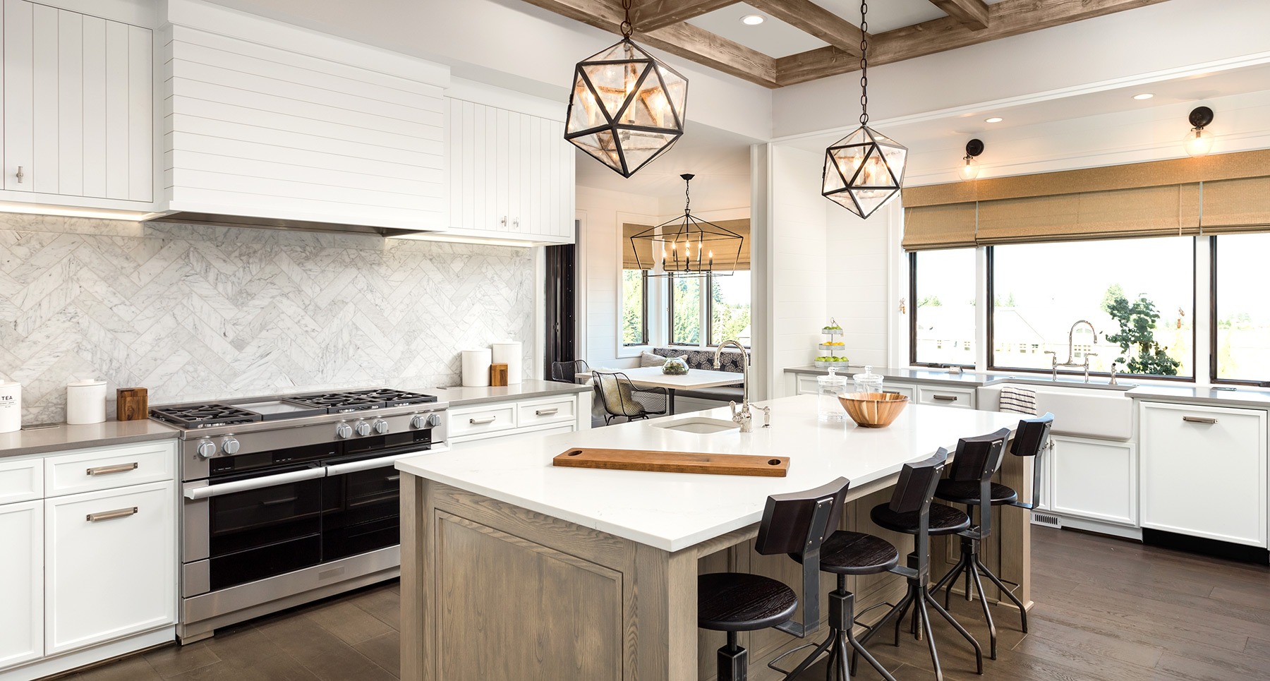 A modern kitchen with a large island, white cabinets, and stainless steel appliances. The kitchen features a white countertop and a sink.