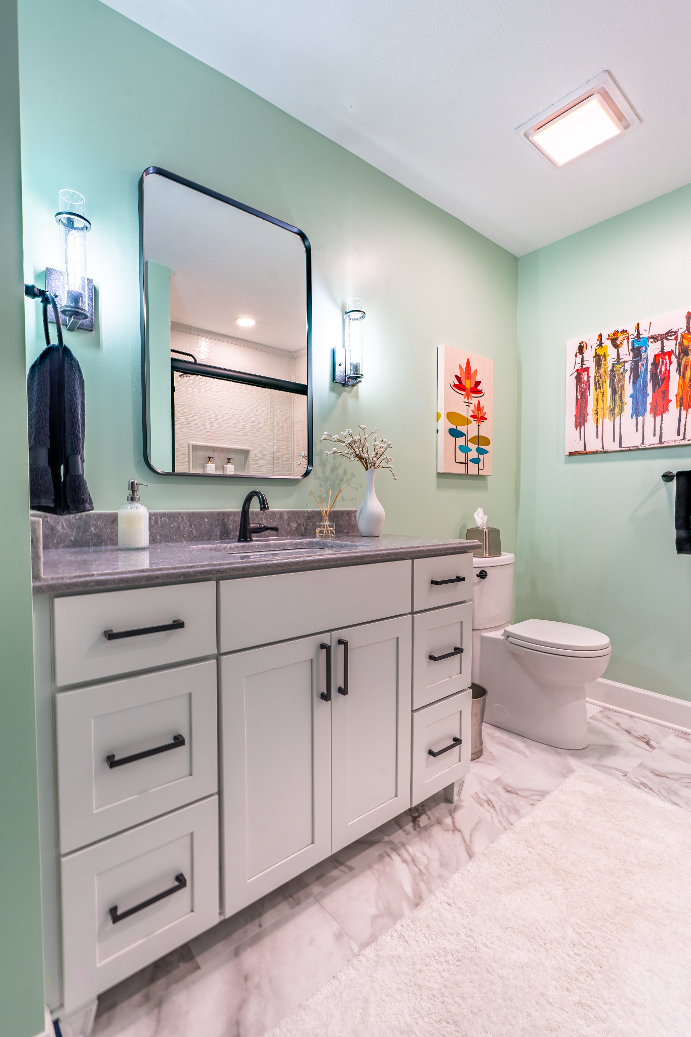 Bathroom interior with green walls, white vanity, and colorful art.