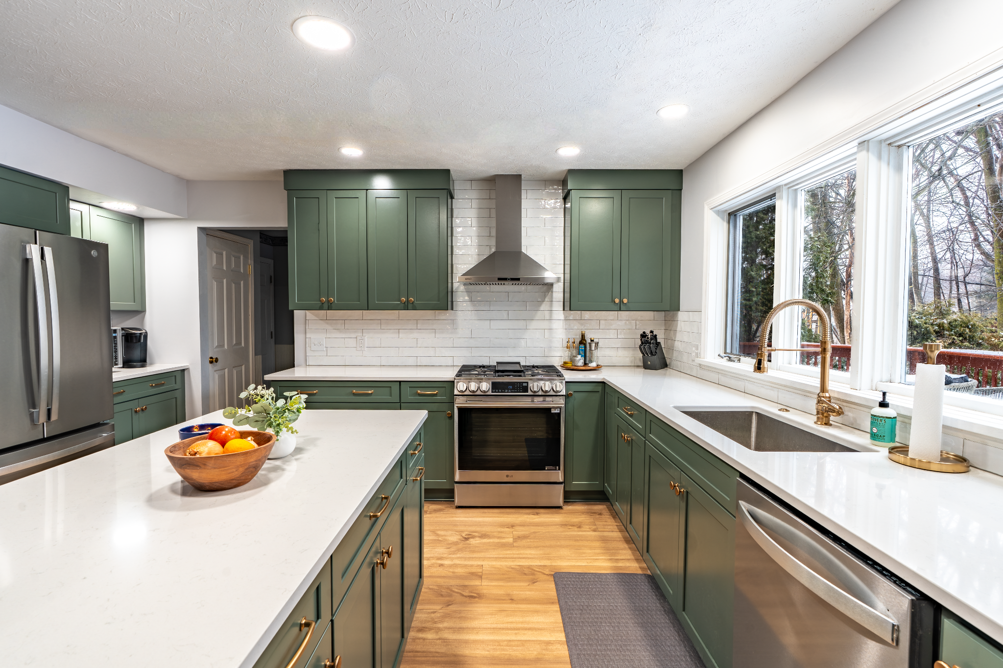 Green kitchen cabinets and white countertops with a bowl of fruit
