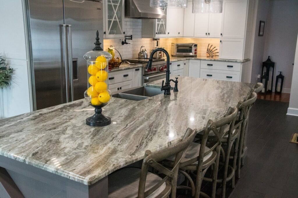 A kitchen island with a marble countertop and yellow decor. The kitchen has white cabinets and stainless steel appliances.