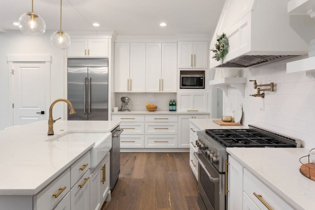 A modern kitchen with white cabinets and gold fixtures. The kitchen features a large island with a sink and a gas stove.