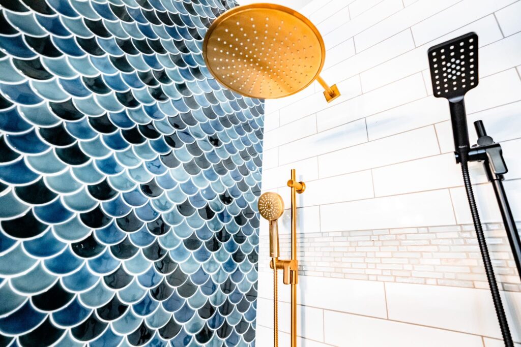 Modern shower with blue fish scale tiles and gold fixtures. Black handheld showerhead on right.