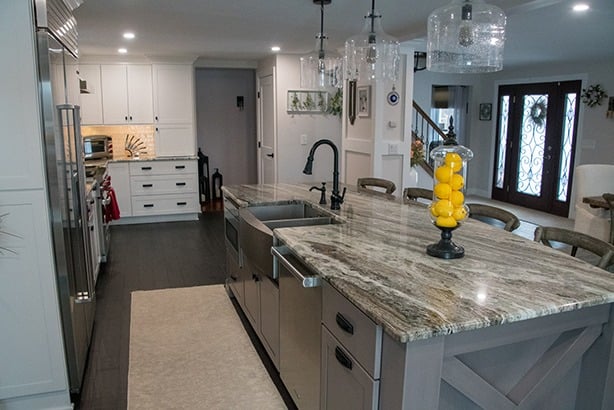 A modern kitchen with a large marble island and stainless steel appliances. The kitchen is well-lit and features a sink and a yellow decorative item on the island.
