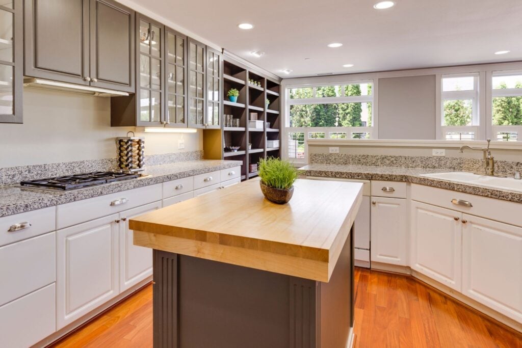 A modern kitchen with white cabinets and a large island. The kitchen has a sink and a window with a view.