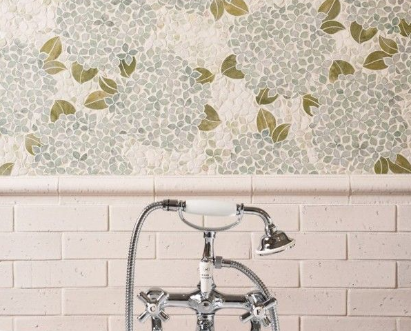 A bathroom faucet with a shiny chrome finish. The faucet is mounted on a white subway tile wall with a decorative mosaic tile backsplash.