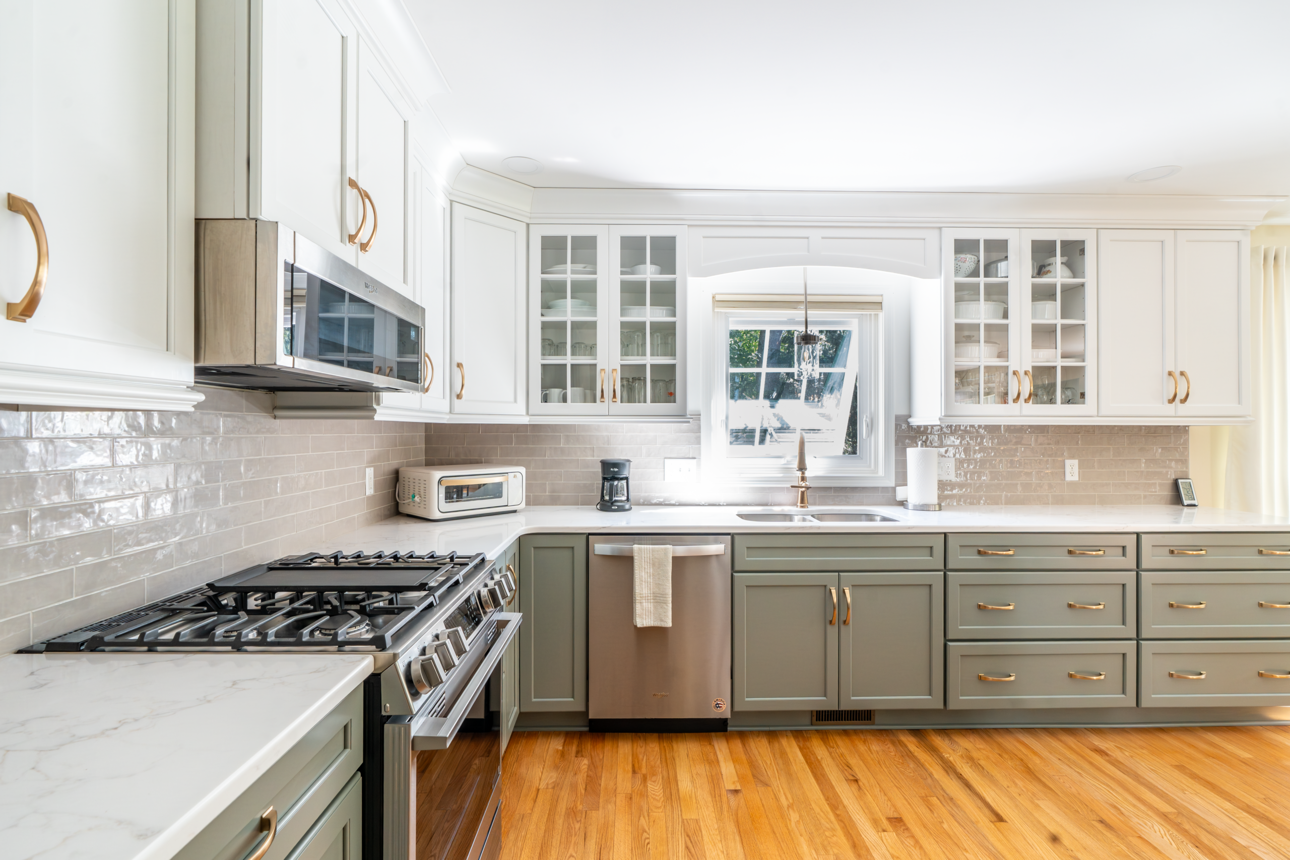 A modern kitchen featuring white and beige cabinets, marble countertops, and stainless steel appliances.