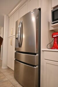 A stainless steel French door refrigerator integrated into white kitchen cabinetry next to a red mixer and microwave.