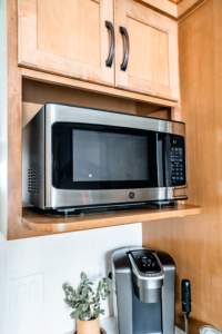 A stainless steel microwave mounted under a light wood kitchen cabinet next to a coffee maker.
