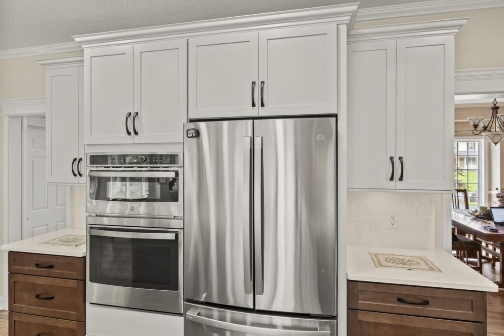 Elegant kitchen featuring white shaker-style upper cabinets, stainless steel refrigerator and oven, and wood base drawers.