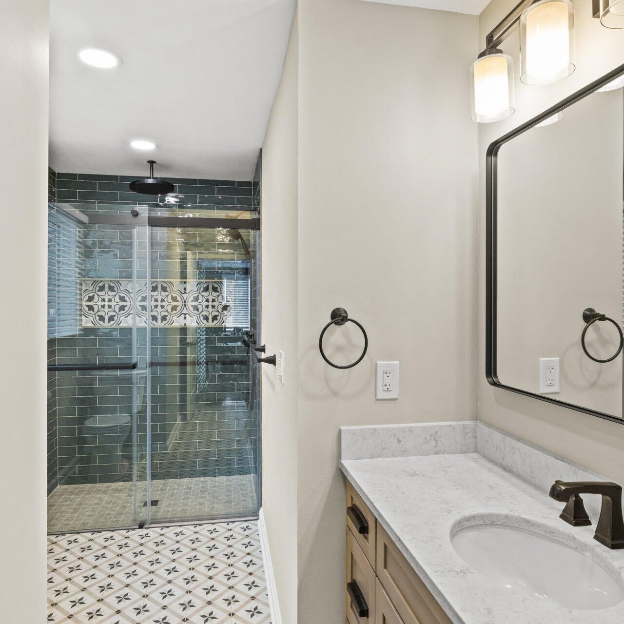 A modern bathroom with a marble countertop, rectangular mirror, wall-mounted lights, and a walk-in shower featuring green subway tiles—perfect inspiration for your next kitchen remodel. Decorative accent tiles add style to the floor and shower wall. A modern bathroom with a marble countertop, rectangular mirror, wall-mounted lights, and a walk-in shower featuring green subway tiles—perfect inspiration for your next kitchen remodel. Decorative accent tiles add style to the floor and shower wall.