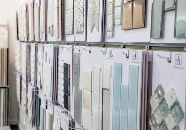 The Webster Showroom wall displays various tile samples in different shapes, colors, and patterns on white boards, arranged neatly in rows above a wooden floor.