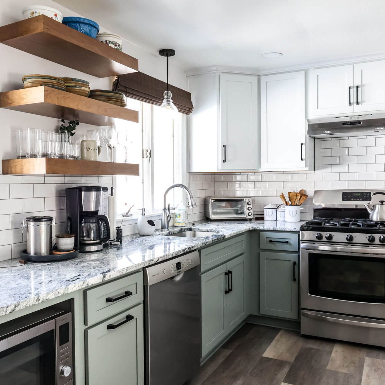 Modern kitchen remodel with white upper cabinets, light green lower cabinets, stainless steel appliances, open wooden shelves for dishes, and a marble countertop. Subway tile backsplash and a large window create a bright atmosphere. Modern kitchen remodel with white upper cabinets, light green lower cabinets, stainless steel appliances, open wooden shelves for dishes, and a marble countertop. Subway tile backsplash and a large window create a bright atmosphere.