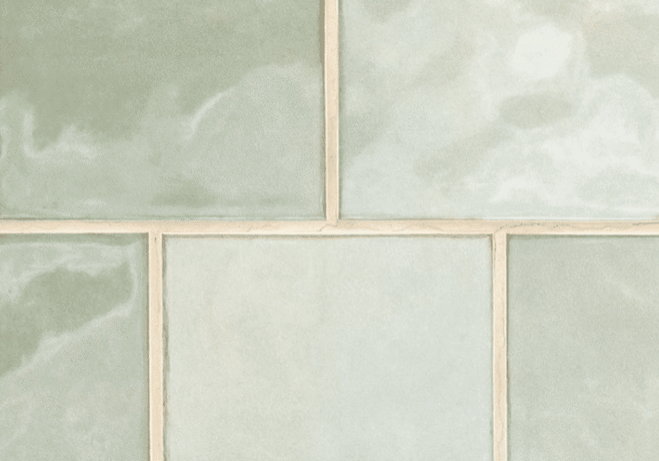 A close-up of six pale green, glossy ceramic tiles with cream-colored grout lines, arranged in a grid pattern. Perfect for a kitchen remodel, the tiles have subtle marbled textures and a soft, smooth finish.