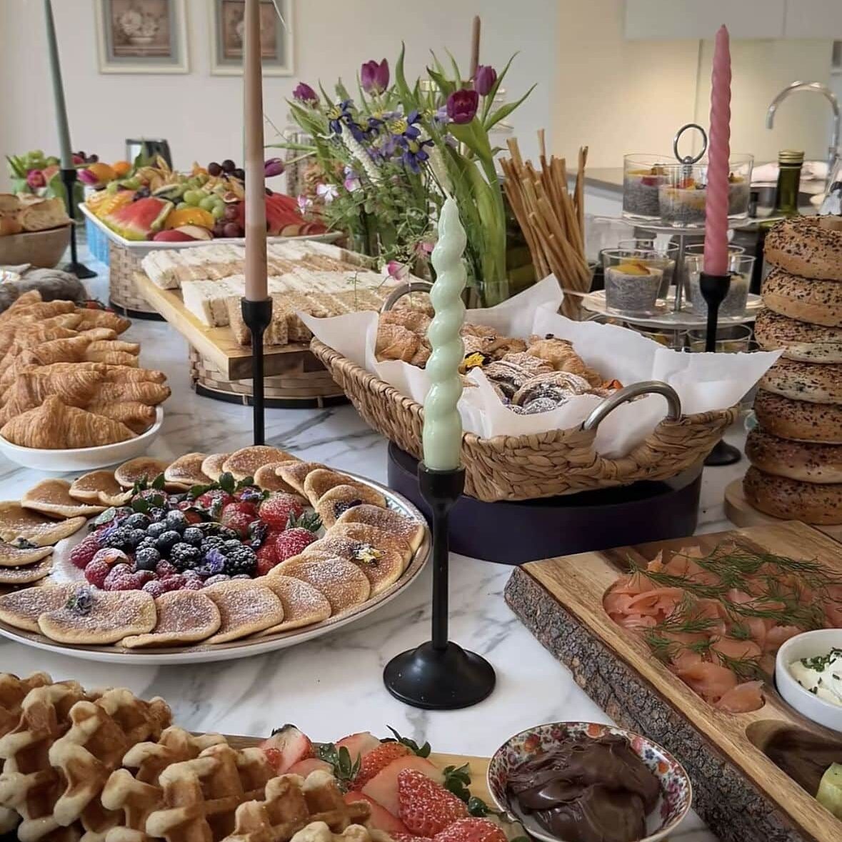 A spread of breakfast foods including waffles, pastries and fruit. The table is set with various dishes and decorations.
