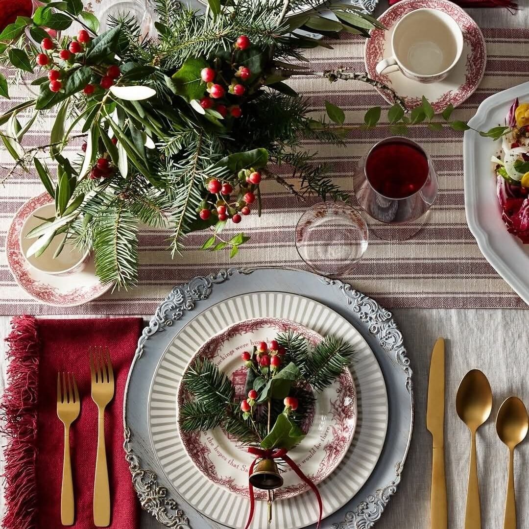 A beautifully set table with plates, gold cutlery, and a festive Christmas arrangement.
