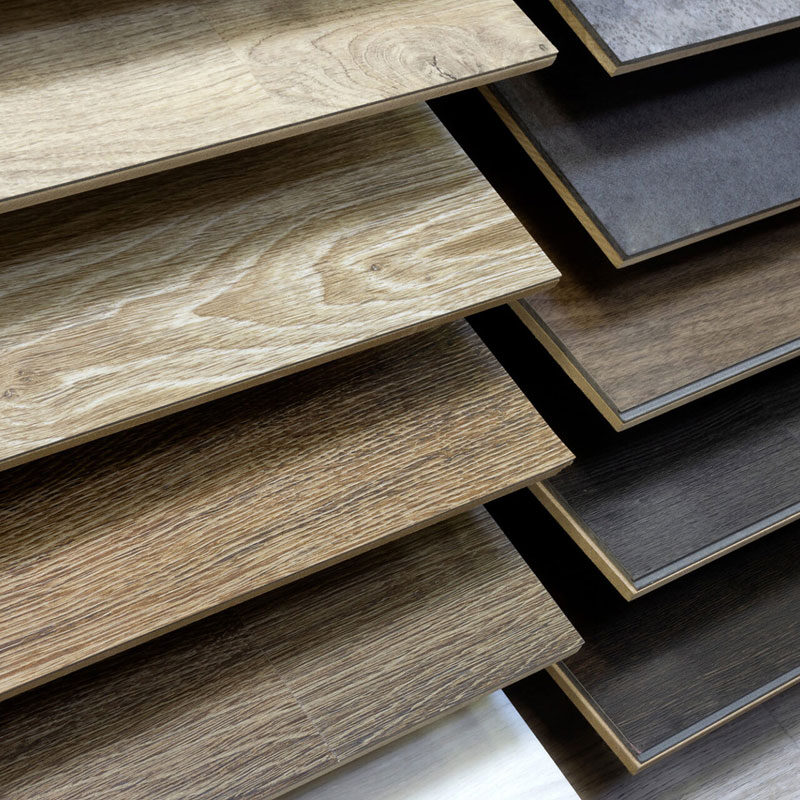 Several samples of waterproof flooring are displayed in rows, showcasing a variety of wood grain patterns and colors, ranging from light tan to dark brown and gray.