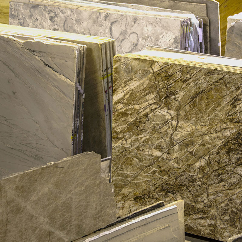 Several large slabs of natural stone, including marble and granite, are vertically displayed side by side in a showroom, highlighting various colors and veined patterns perfect for elegant flooring or water resistant flooring solutions.